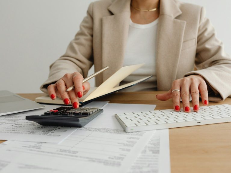 Eine Person mit roten Nägeln blättert in einem Dokument auf einem Schreibtisch.